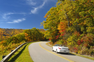 A couple in a white convertible car enjoys the wamr October fall day in the mountains on Blue Ride Parkway in North Carolina, USA.